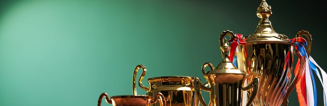 Trophies from small to big lined up in front of a green backdrop